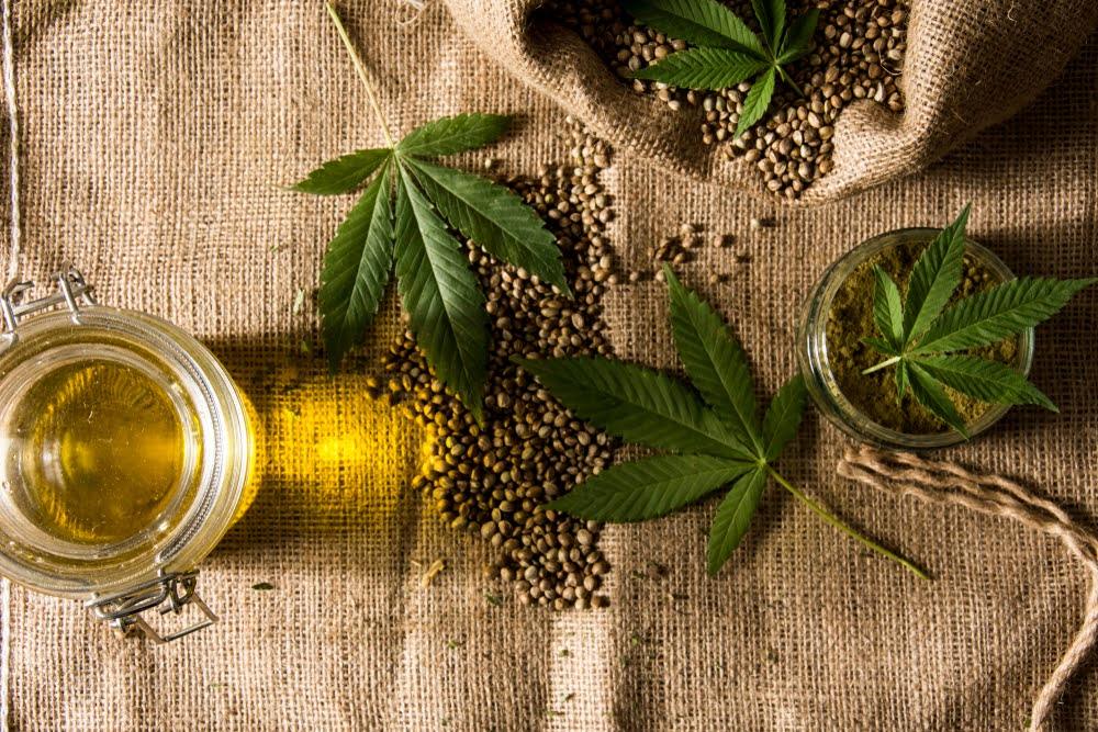 Hemp leaves, hemp seeds, and jars of hemp oil on burlap fabric