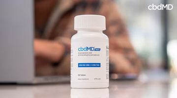 CBD supplement bottle with dosage label on a table, person blurred in background