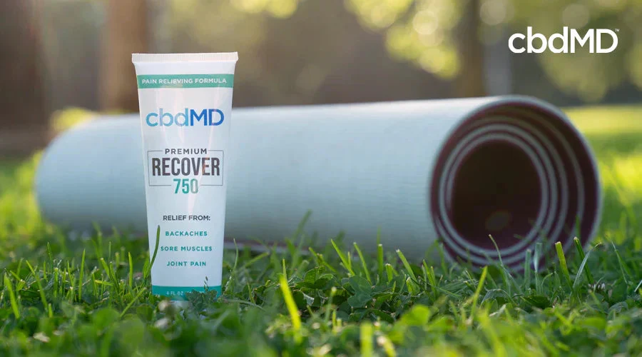 Tube of pain relief cream on grass beside a rolled yoga mat outdoors
