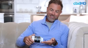 Smiling man on sofa pouring cbd capsules into hand in a bright home setting