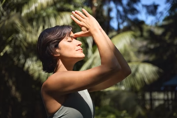 Woman practicing deep breathing exercise outdoors in nature with sunlight and palm trees
