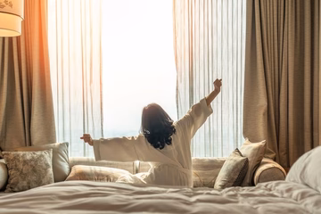 Woman stretching in bed by window with morning sunlight, wellness and relaxation concept