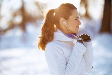 Woman running outdoors in winter, wearing earphones and a white jacket, snow background