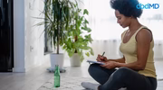 Woman sitting on floor writing healthy new year resolutions, water bottle and plant nearby